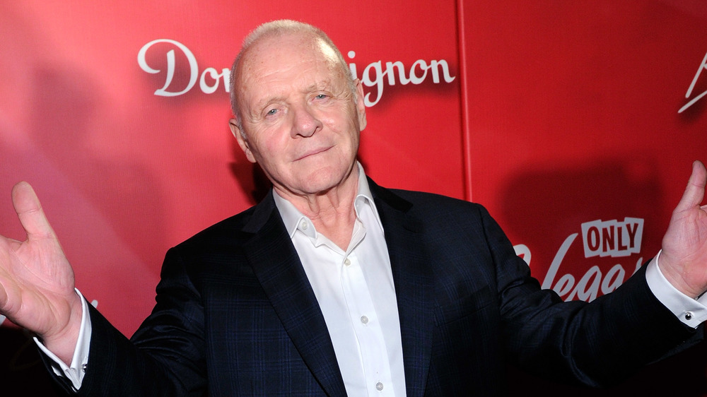 Anthony Hopkins, not smiling, arms up, shrugging, red carpet