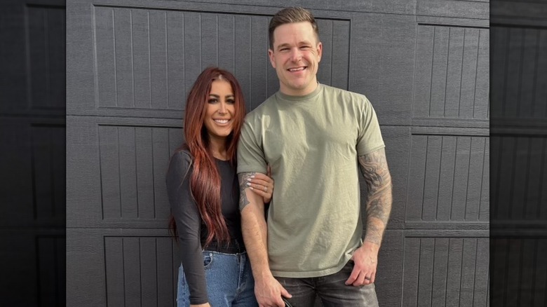 Chelsea DeBoer wearing a charcoal gray long-sleeved shirt and gripping the upper arm of Cole DeBoer, who wears a light green T-shirt.