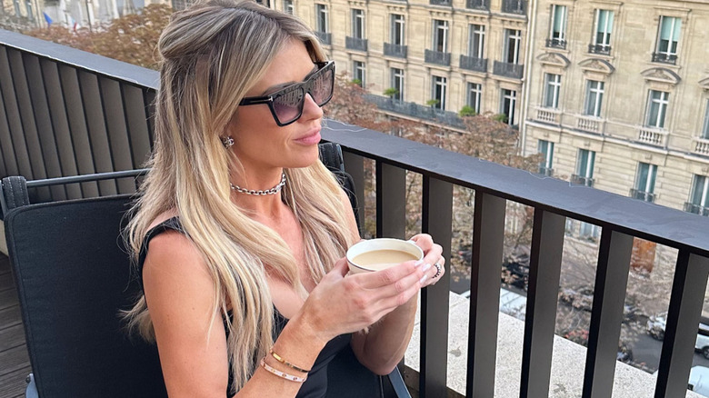 Christina Hall holding a coffee while looking off a balcony in Paris, France