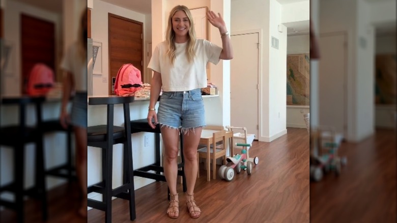 Jasmine Roth waving in a white cropped T-shirt and cut-off jean shorts.