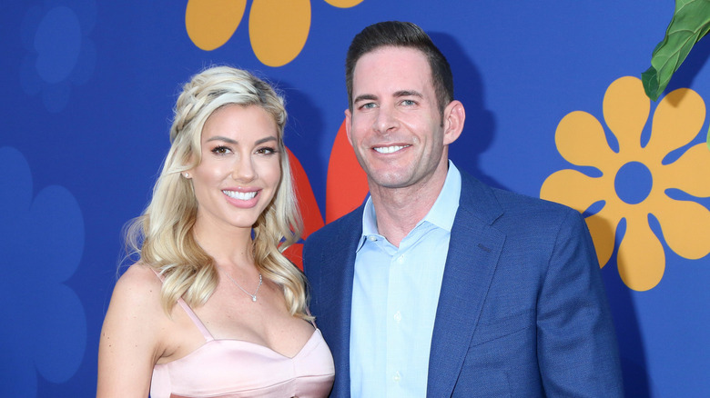 Tarek El Moussa and Heather Rae Young sport beaming smiles against a blue background