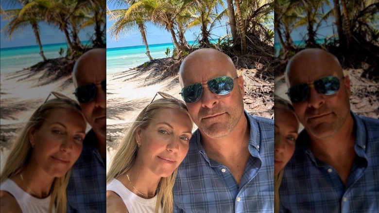 Sarah Baeumler leaning her head on Bryan Baeumler's shoulder with a beach and palm trees behind them.