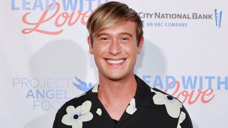 Wearing a patterned shirt Tyler Henry looks into the camera while smiling joyfully