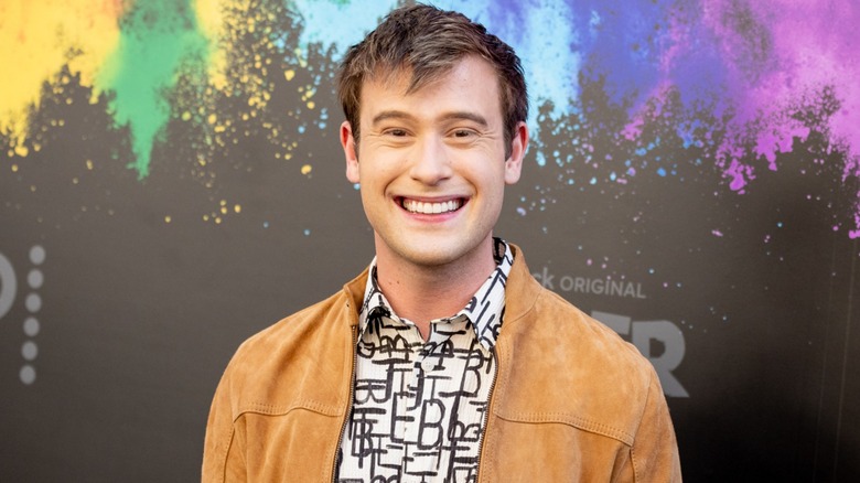 Wearing a brown jacket and a patterned shirt Tyler Henry flashes a bright smile