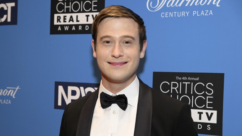 Wearing a black tuxedo with a matching black bow tie, Tyler Henry gives a soft smile