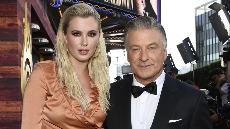 Ireland Baldwin and Alec Baldwin stand close to each other as they look directly into the camera.