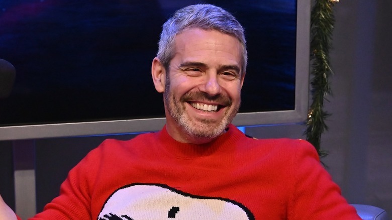 Andy Cohen smiling and holding a microphone