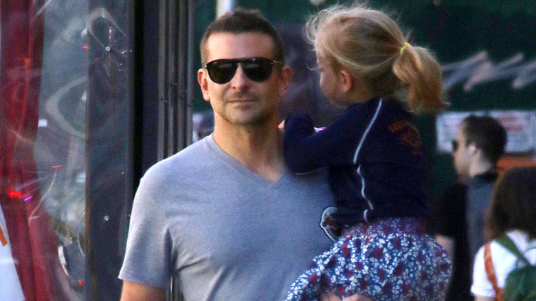 Bradley Cooper holding his daughter and walking 