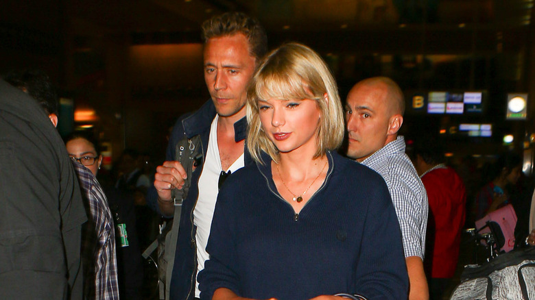 Tom Hiddleston frowning behind Taylor Swift