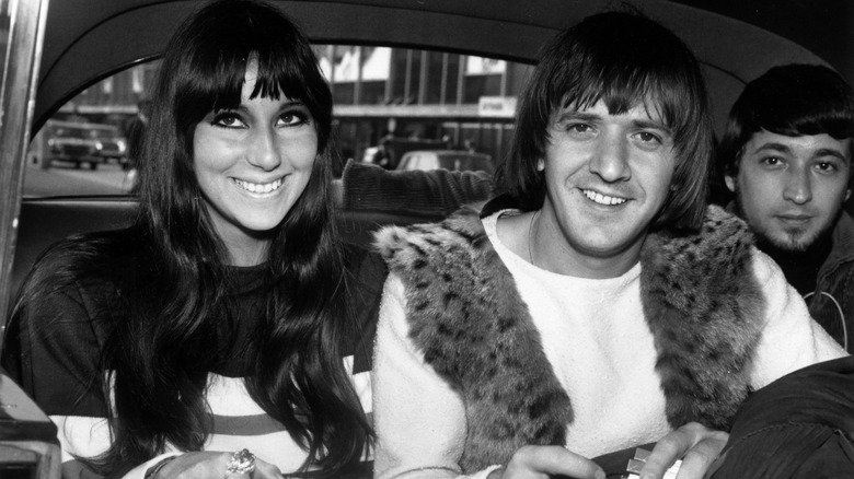 Cher and Sonny Bono smiling while sitting in a car with another man