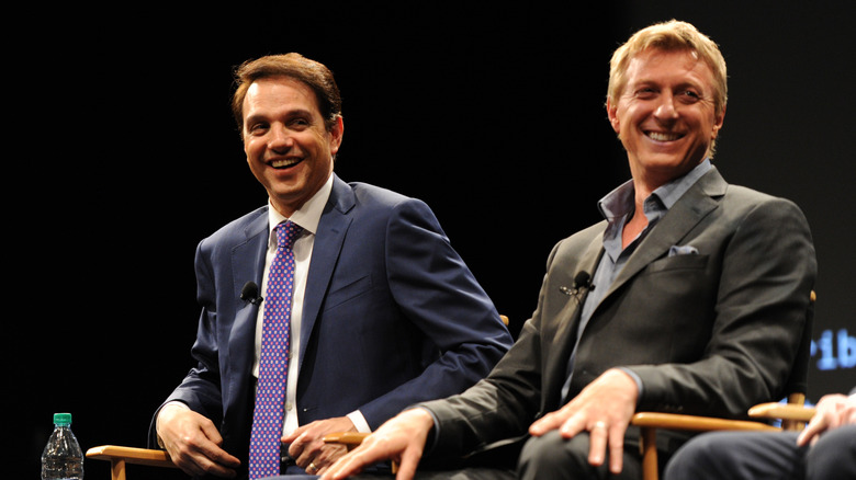 Ralph Macchio and William Zabka sitting in chairs and laughing