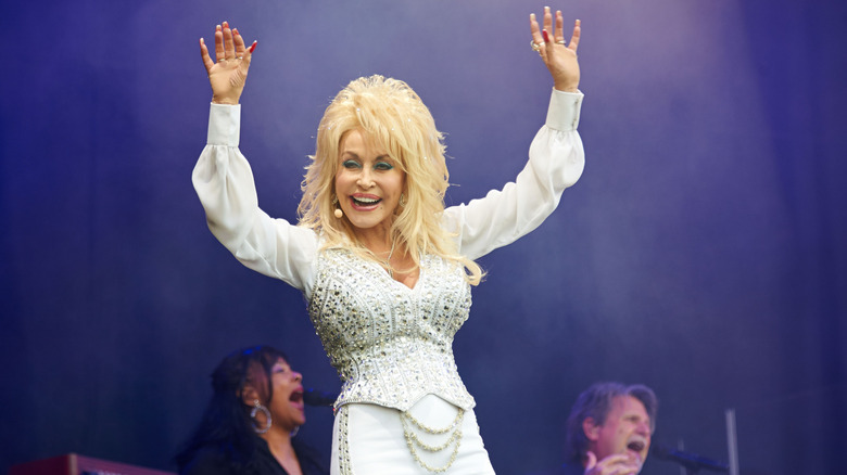 Dolly Parton waving and smiling onstage in a sparkly white outfit at Glastonbury 2014