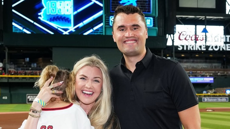 Erika and Charlie Kirk pose with their daughter at a baseball game