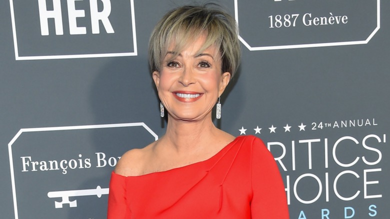 Sporting a red dress that exposes one shoulder, Annie Potts smiles hard at the camera.