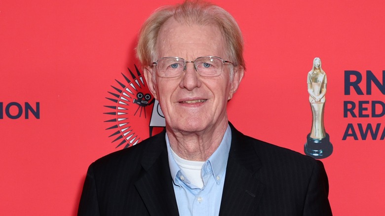 Wearing a set of glasses and a casual suit, Ed Begley Jr. looks directly at the camera while sporting a light smile.