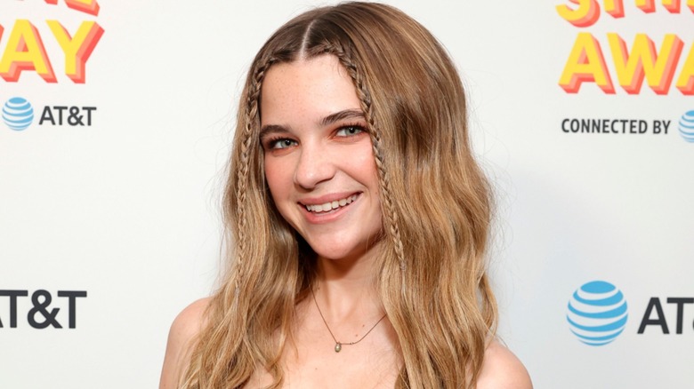 Sporting partly braided hair, Raegan Revord tilts her head to the side and wears a wide smile.