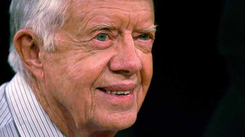 Jimmy Carter smiles in front of black background.
