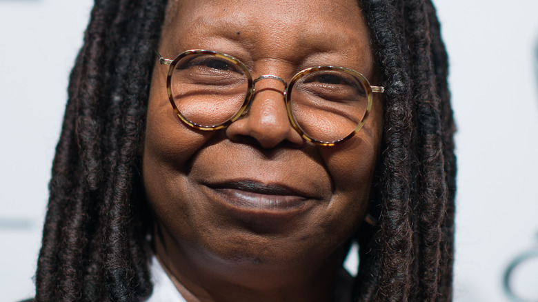 Whoopi Goldberg smiles in tortoise shell glasses.