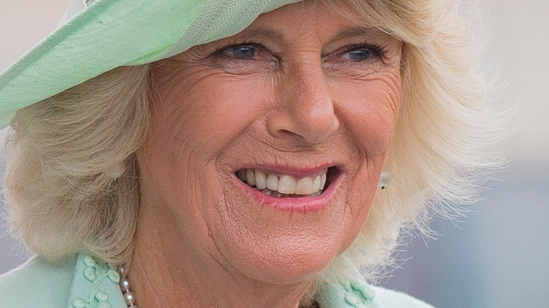 Camilla Parker Bowles smiling and wearing seafoam hat