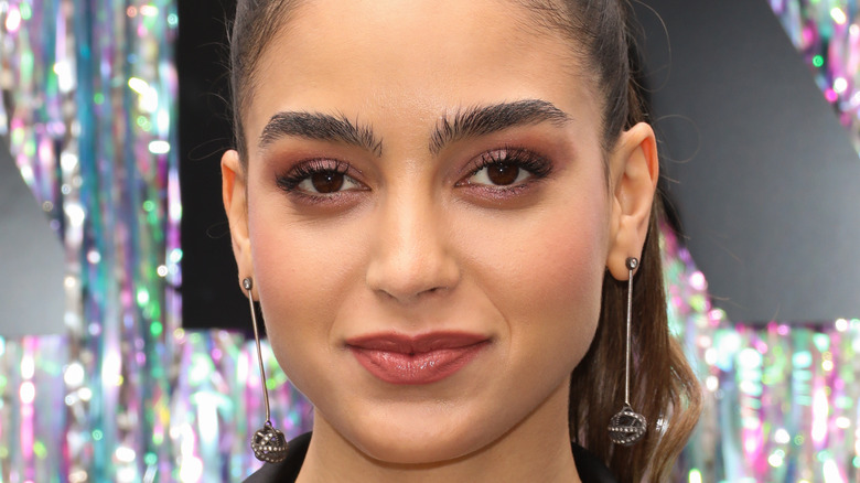 Melissa Barrera, smiling with no teeth, 2019 red carpet, hair in pony tail, wearing earrings