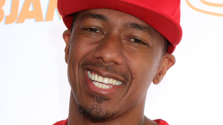 Nick Cannon wears a red baseball hat and smiles