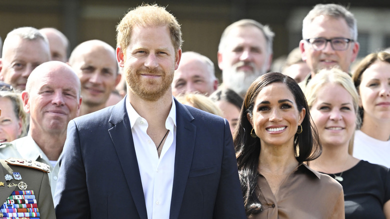 Prince Harry and Meghan Markle smiling in a crowd.