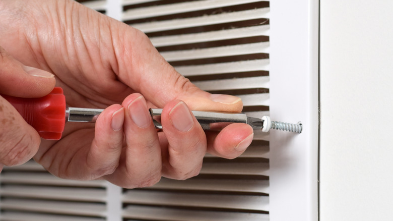 Hand holding a screwdriver, unscrewing an air vent