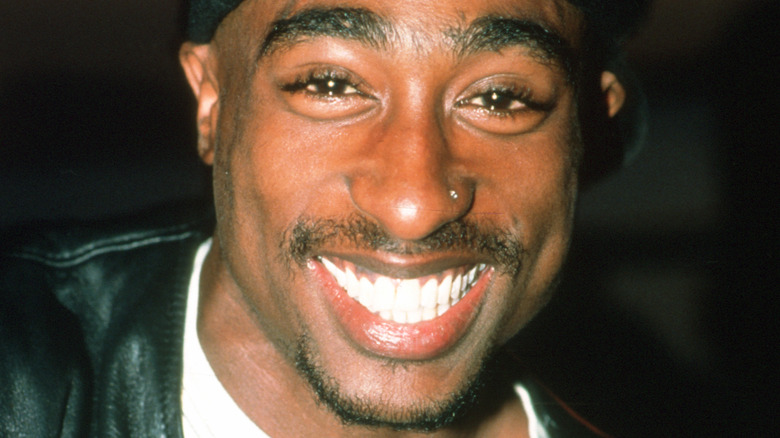 Tupac Shakur smiles wearing a black cap.