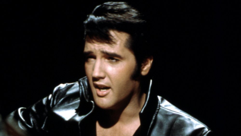 Elvis Presley playing guitar and wearing a black leather jacket