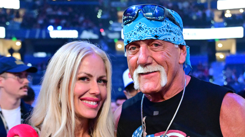 Hulk Hogan wearing a black shirt and blue bandana while posing next to his wife Sky Daily