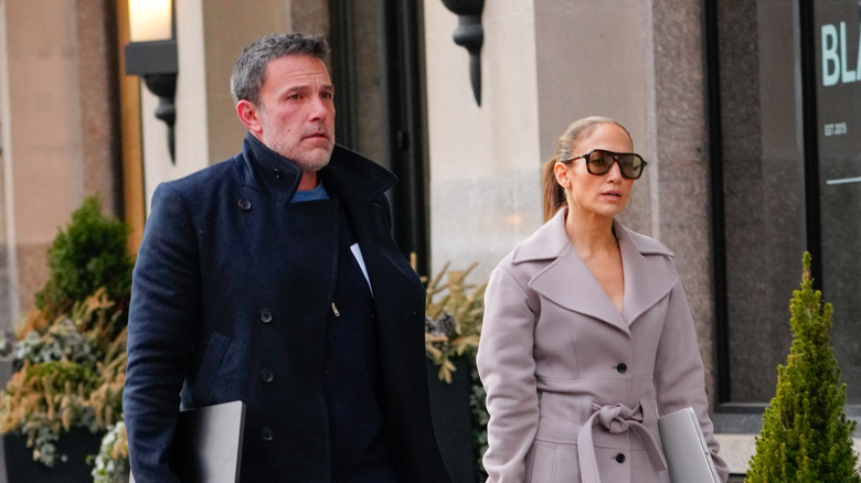 Jennifer Lopez wearing a trench coat and sunglasses walking with Ben Affleck wearing a blue coat.