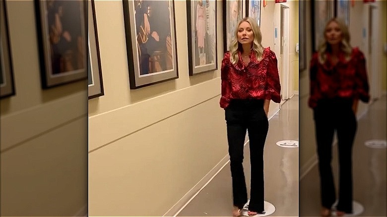 Kelly Ripa in a hallway with dark trousers and a red blouse in 2021