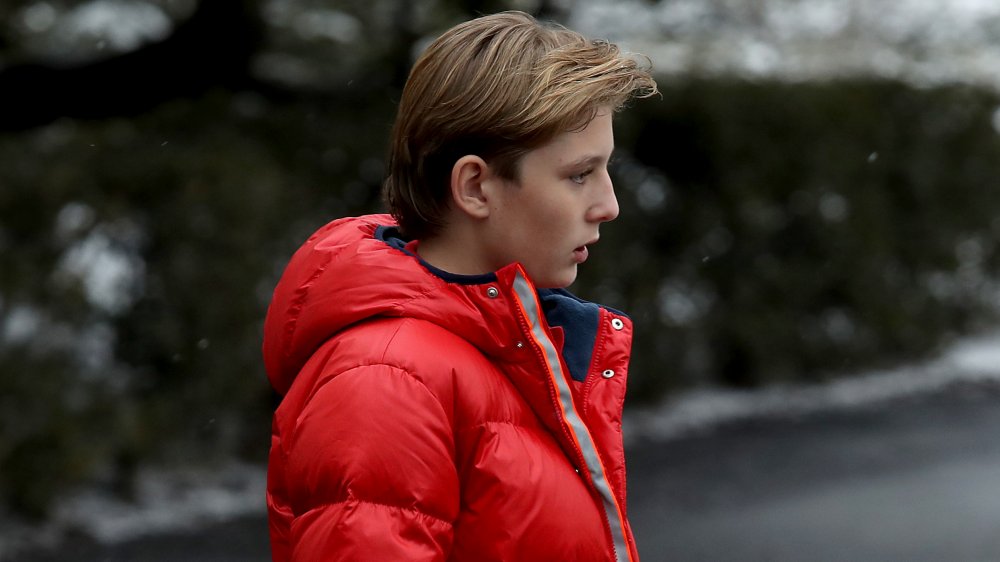Profile of Barron Trump walking outside in a red jacket