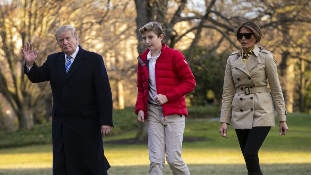 Donald Trump waving while walking alongside Barron and Melania Trump outside