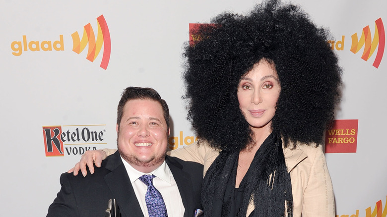 Chaz Bono posing with mom Cher, who's wearing a large afro-style wig