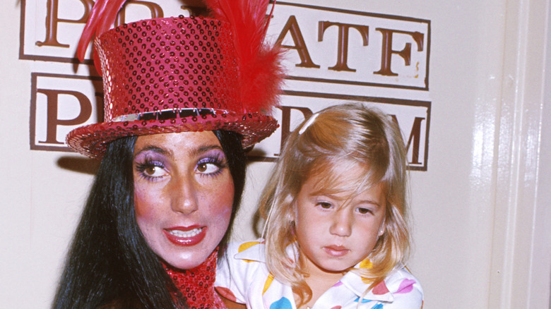 Cher wearing a pink top hat while posing with young Chaz Bono