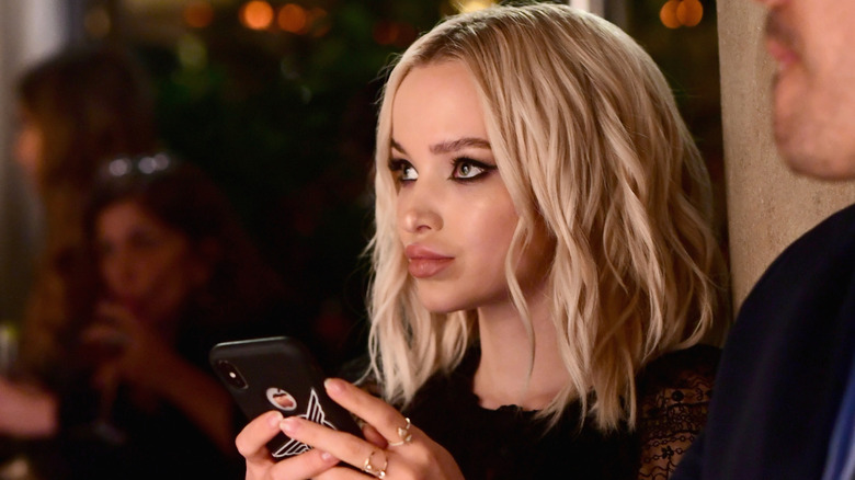 Dove Cameron looking ahead and holding her phone