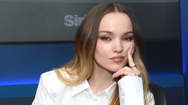Dove Cameron with her fingers on her cheek while posing in SiriusXM studio