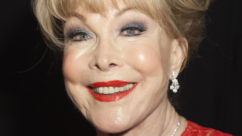 Barbara Eden smiles in a red outfit and lipstick