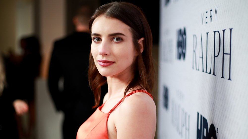 Emma Roberts in a red dress with brunette hair, posing from the side at a step-and-repeat