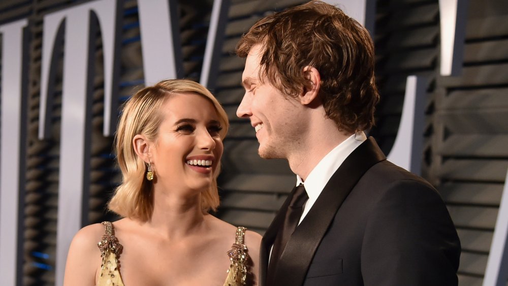 Emma Roberts in a gold dress and Evan Peters in a black suit, smiling at each other on the red carpet
