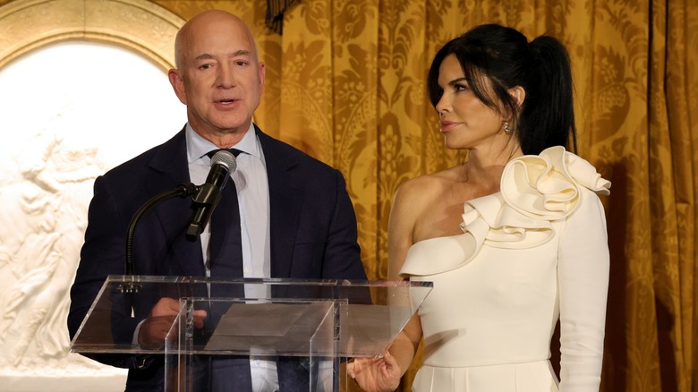 Lauren Sanchez looks at Jeff Bezos, who is speaking into a microphone.