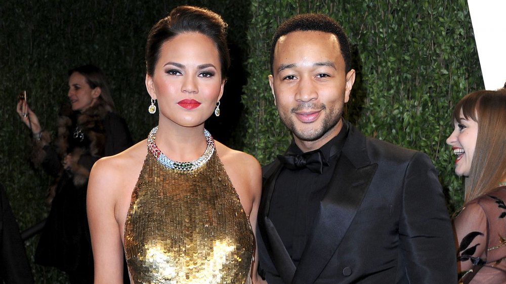 Chrissy Teigen in a gold gown standing with John Legend