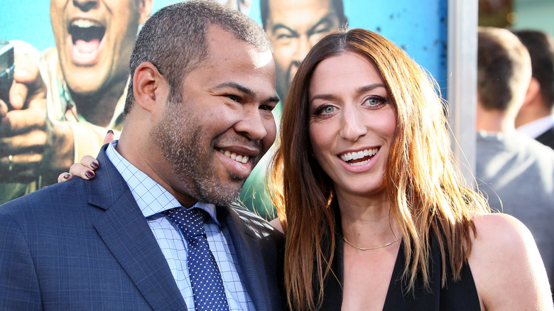 Jordan Peele in a blue suit, Chelsea Peretti in a black dress, both smiling big