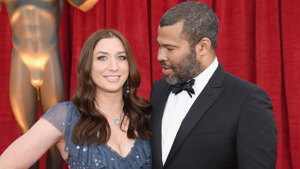 Chelsea Peretti smiling in a blue dress, Jordan Peele in a black suit looking at her