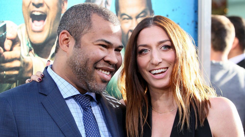 Jordan Peele in a blue suit, Chelsea Peretti in a black dress, both smiling big