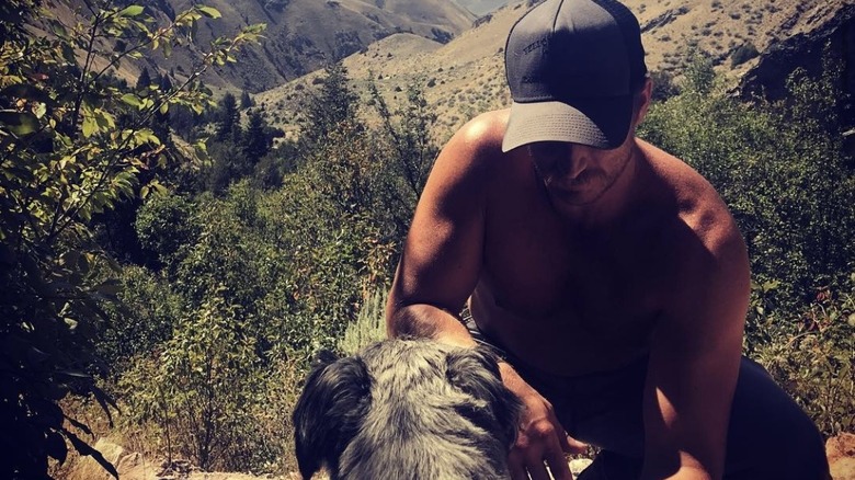 Kyle Baugher, shirtless, in nature, hiding his face