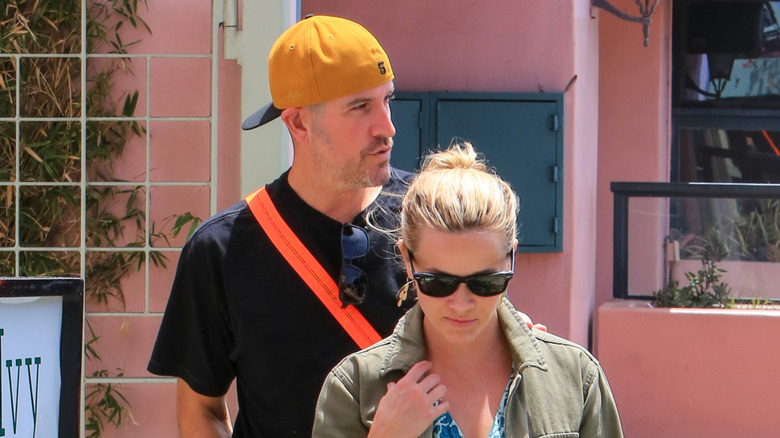 Jim Toth wearing a black t-shirt and backwards yellow baseball hat and Reese Witherspoon wearing a green denim jacket and blue floral dress