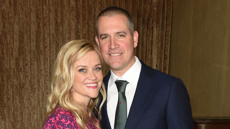 Reese Witherspoon wearing a pink floral top with Jim Toth wearing a blue suit and grey-silver tie