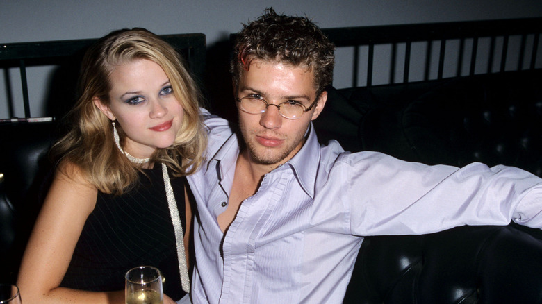 Reese Witherspoon wearing a black sleeveless dress and white neck ribbon and Ryan Phillippe wearing an open collared shirt and glasses